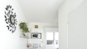 Une cuisine compacte avec des meubles blancs, un four à micro-ondes, un petit réfrigérateur et une fenêtre offrant une vue.