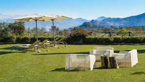 A grassy outdoor area with sun loungers and umbrellas, a table, and chairs. - Villa Coco - 10 Guests, Stunning Mt Etna Views (Castiglione di Sicilia)