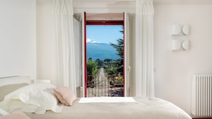 A bedroom with a bed, a view of a mountain through an open door, and a radiator on the wall. - Villa Coco - 10 Guests, Stunning Mt Etna Views (Castiglione di Sicilia)