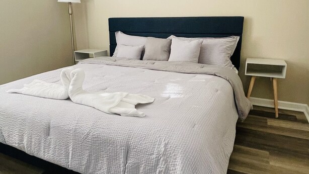 Un lit bien fait, avec une couette blanche et des oreillers, une lampe de chevet, une petite table de chevet et un tableau accroché au mur.