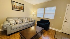 Un salon avec un canapé gris, un fauteuil foncé, une table basse et un tableau accroché au mur.