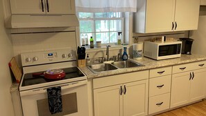Una cucina con mobili bianchi, un fornello, un forno a microonde e un lavandino.