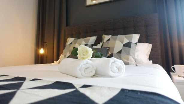 A neatly made bed with rolled towels and a white rose, a geometric-patterned pillow, and a framed picture on the wall. - Em-charming Apartment (Ponta Delgada)