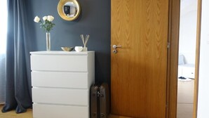 A room with a white dresser, a mirror, a vase with flowers, a bowl, and a set of incense sticks. There is a wooden door and a suitcase on the floor. - Em-charming Apartment (Ponta Delgada)