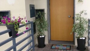 A wooden deck with a metal railing, a wooden door, and two potted plants with flowers. - Em-charming Apartment (Ponta Delgada)
