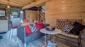 Interior acollidor d'una cabana amb elements de fusta, un sofà, una taula de dinar i una escala que condueix a una zona exterior.