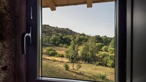 Vista d'una finestra amb sostre de fusta, sobre un paisatge amb turons, arbres i camps oberts.