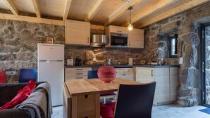 Cuina rústica amb parets de pedra, armaris de fusta i taula de dinar de fusta amb un bol vermell.