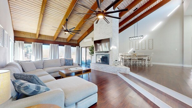 Een ruime woonkamer met een grote hoekbank, een open haard en een eethoek met witte stoelen.