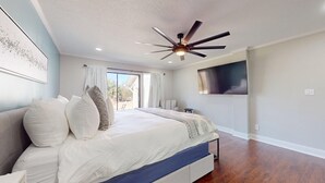 Een slaapkamer met een groot bed, een plafondventilator, een aan de muur bevestigde televisie en uitzicht op de omgeving door een schuifdeur.