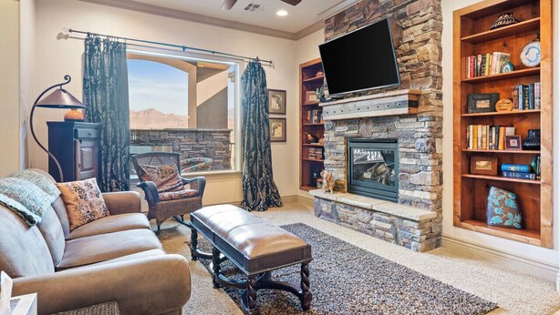 A living room with a stone fireplace, a flat-screen TV, a bookshelf, and a large window with curtains. - Dreamy 2-bedroom condo with sweeping desert views (Hurricane)