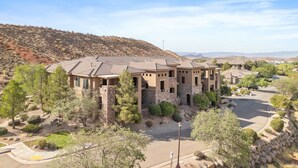 A multi-story building with a stone facade, surrounded by landscaped areas and trees. - Dreamy 2-bedroom condo with sweeping desert views (Hurricane)