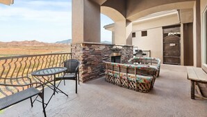 A balcony with a stone fireplace, outdoor seating, and a view of the desert landscape. - Dreamy 2-bedroom condo with sweeping desert views (Hurricane)