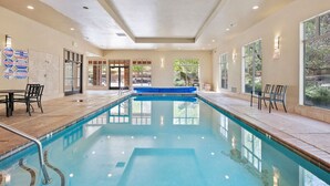 An indoor swimming pool with clear water, surrounded by tiled flooring and walls. There are chairs and tables near the pool, and large windows on one side. - Dreamy 2-bedroom condo with sweeping desert views (Hurricane)