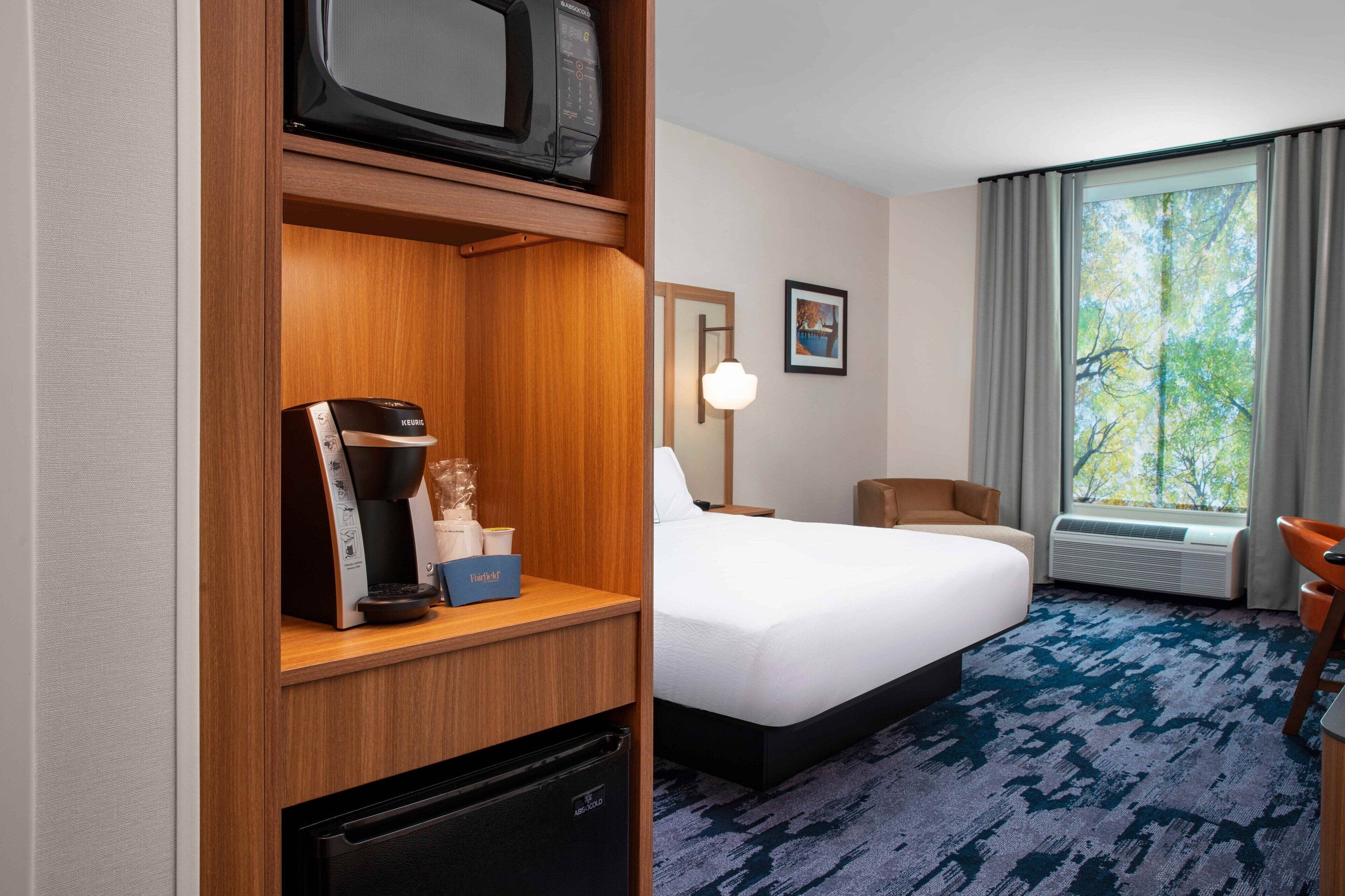 A hotel room with a bed, a desk with a microwave, a coffee maker, and a mini-fridge.