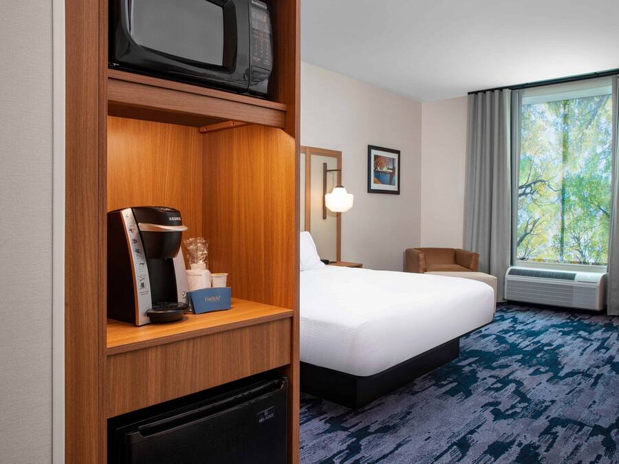 A hotel room with a bed, a desk with a microwave, a coffee maker, and a mini-fridge.
