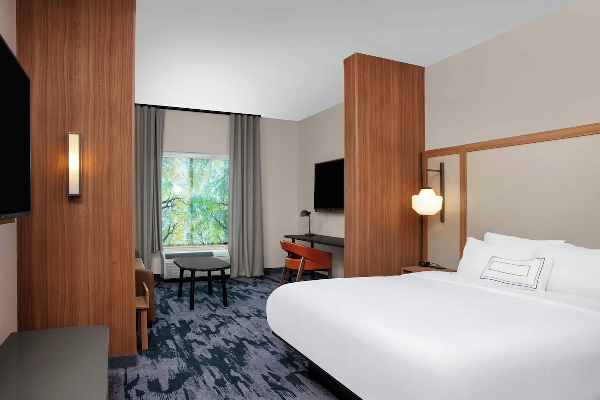 Une chambre d’hôtel avec un grand lit, un bureau avec une chaise, une télévision et une fenêtre avec des rideaux.