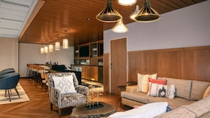 Un salon moderne avec un plafond en bois, un canapé, un fauteuil et des luminaires suspendus.