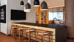 Un espace bar moderne avec un long comptoir, des tabourets en bois et des luminaires suspendus.