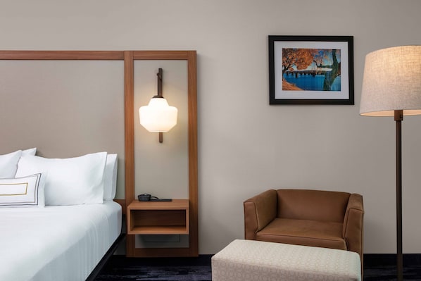 A hotel room with a bed, a nightstand, a lamp, a chair, and a framed picture on the wall.