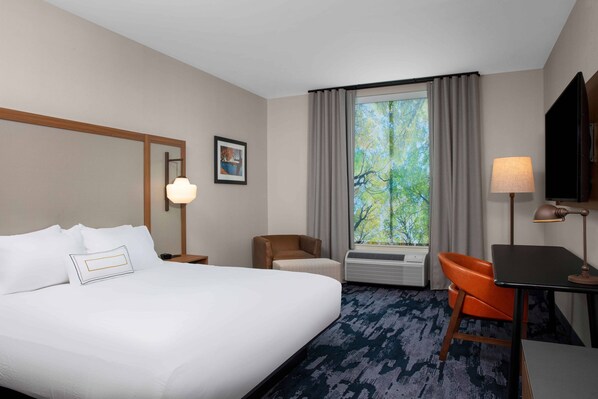 A hotel room with a large bed, a desk, a chair, a window with curtains, a wall-mounted TV, and a framed picture.