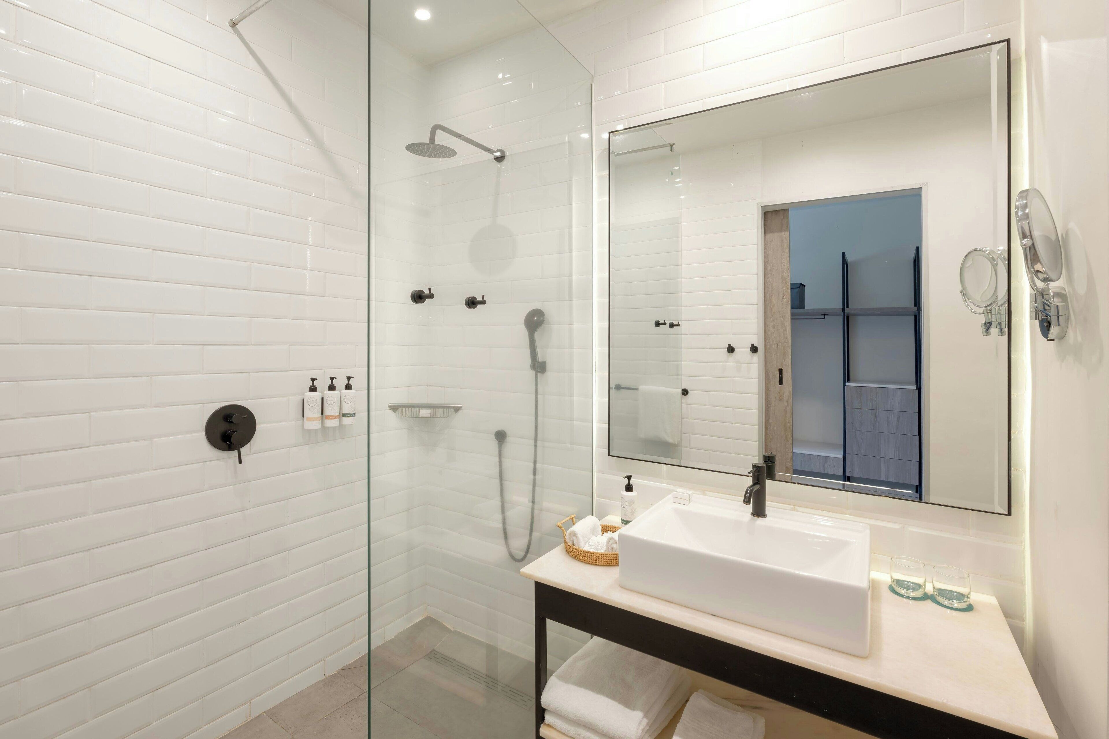 Un bagno moderno con doccia vetrata, uno specchio grande e un lavandino bianco.