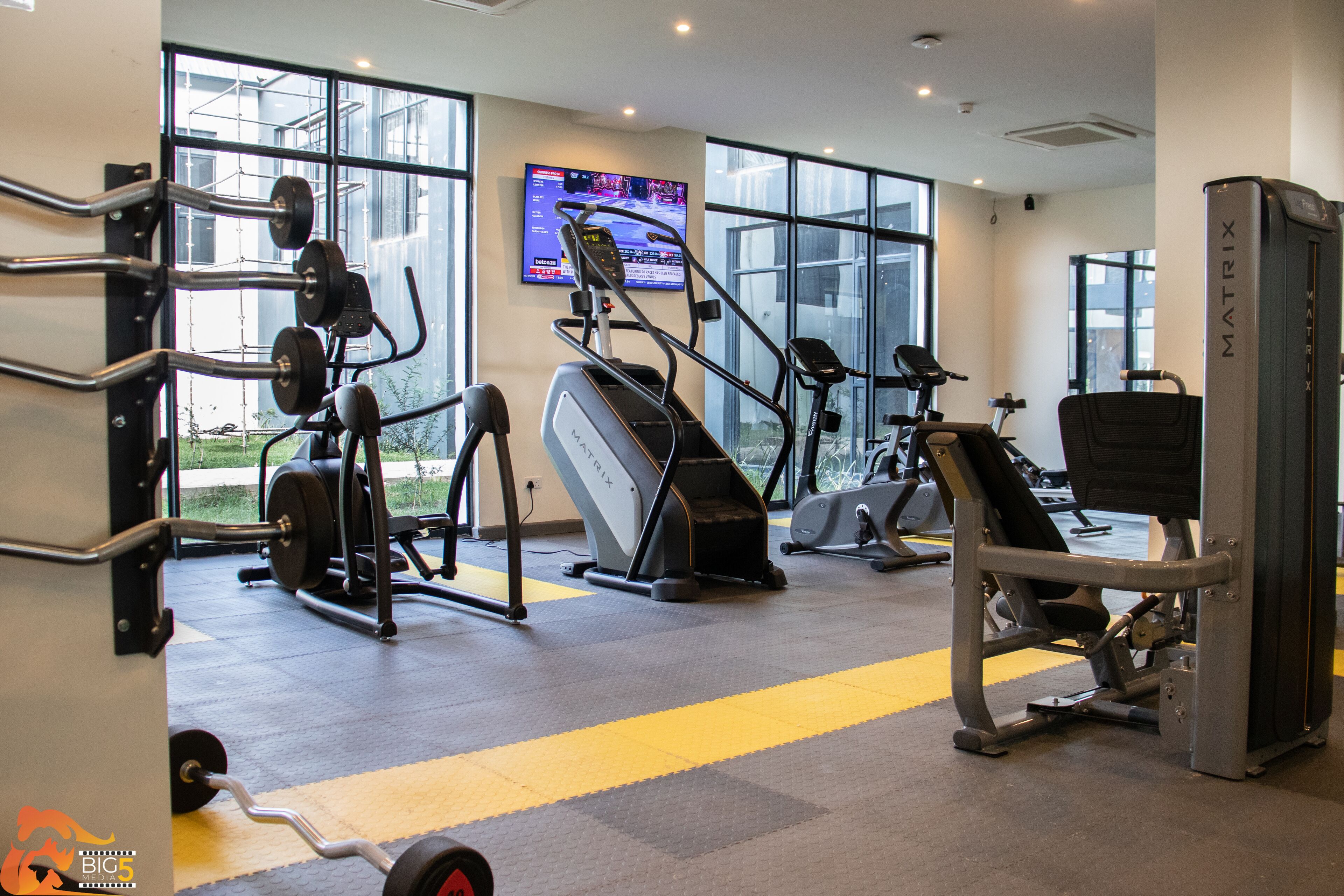 A gym with cardio machines, weightlifting equipment, and a television displaying a workout program.