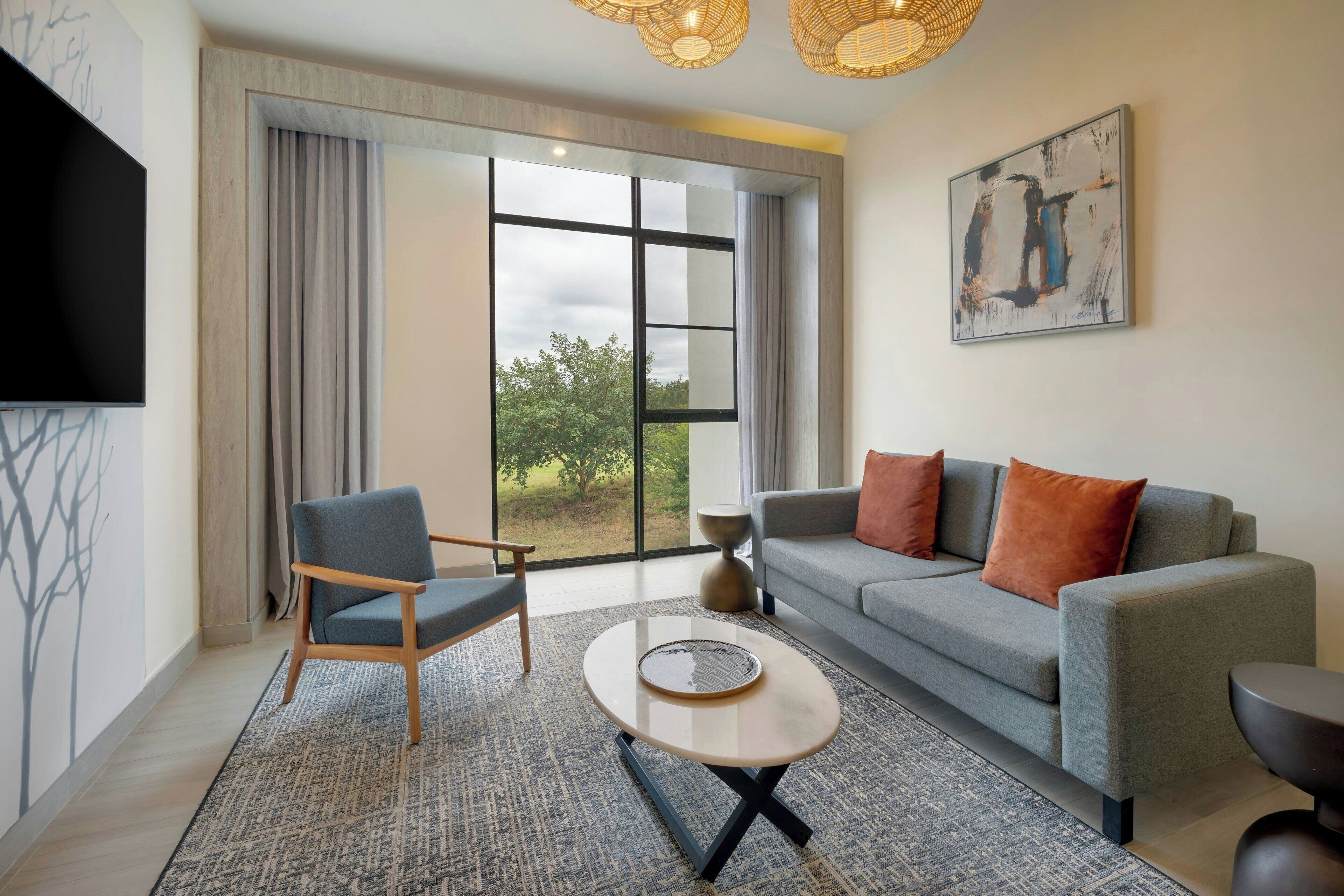 A modern living room with a sofa, armchair, coffee table, and artwork on the wall.