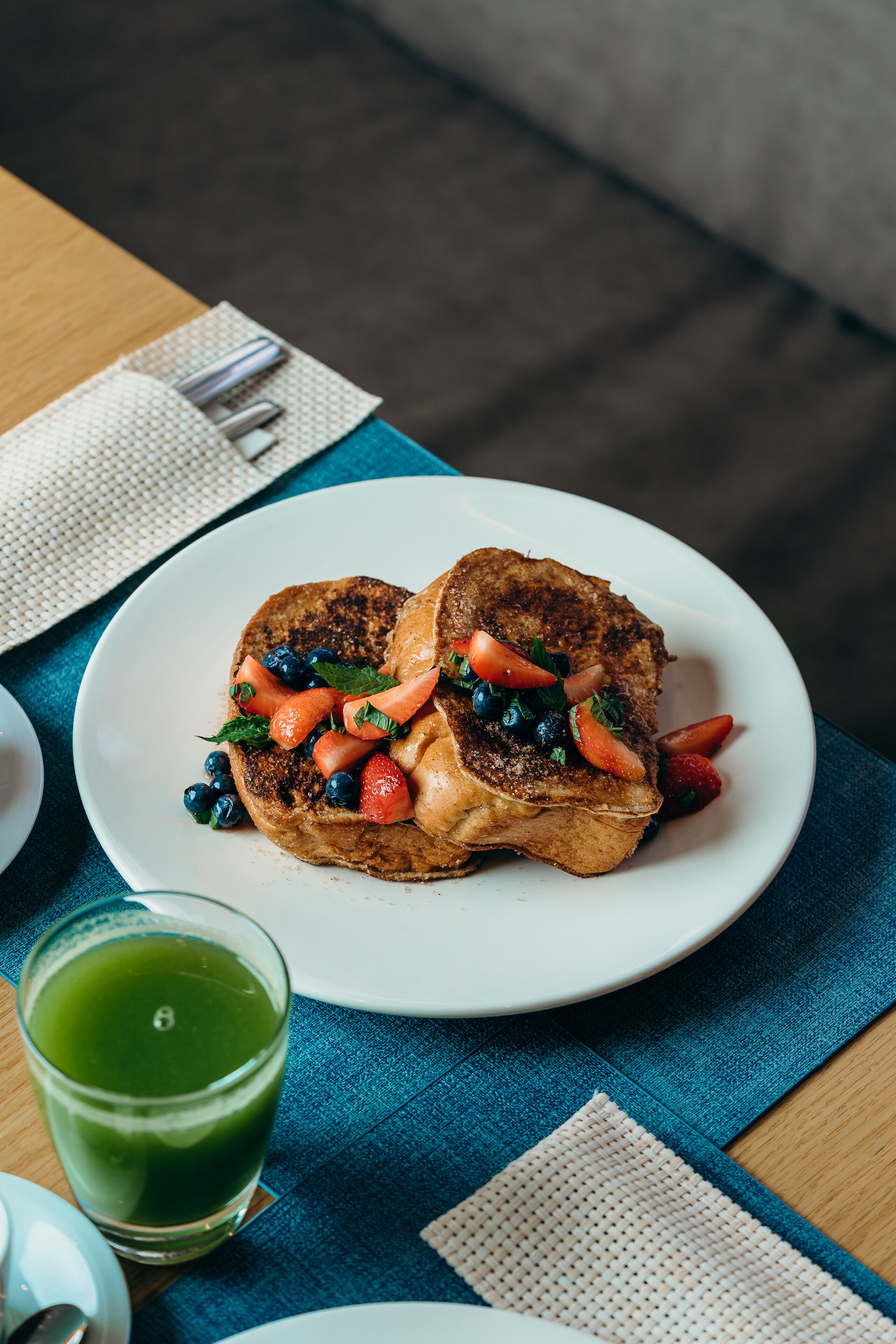 Un plato de panes fritos con frutos rojos y un vaso de té verde sobre una mesa.