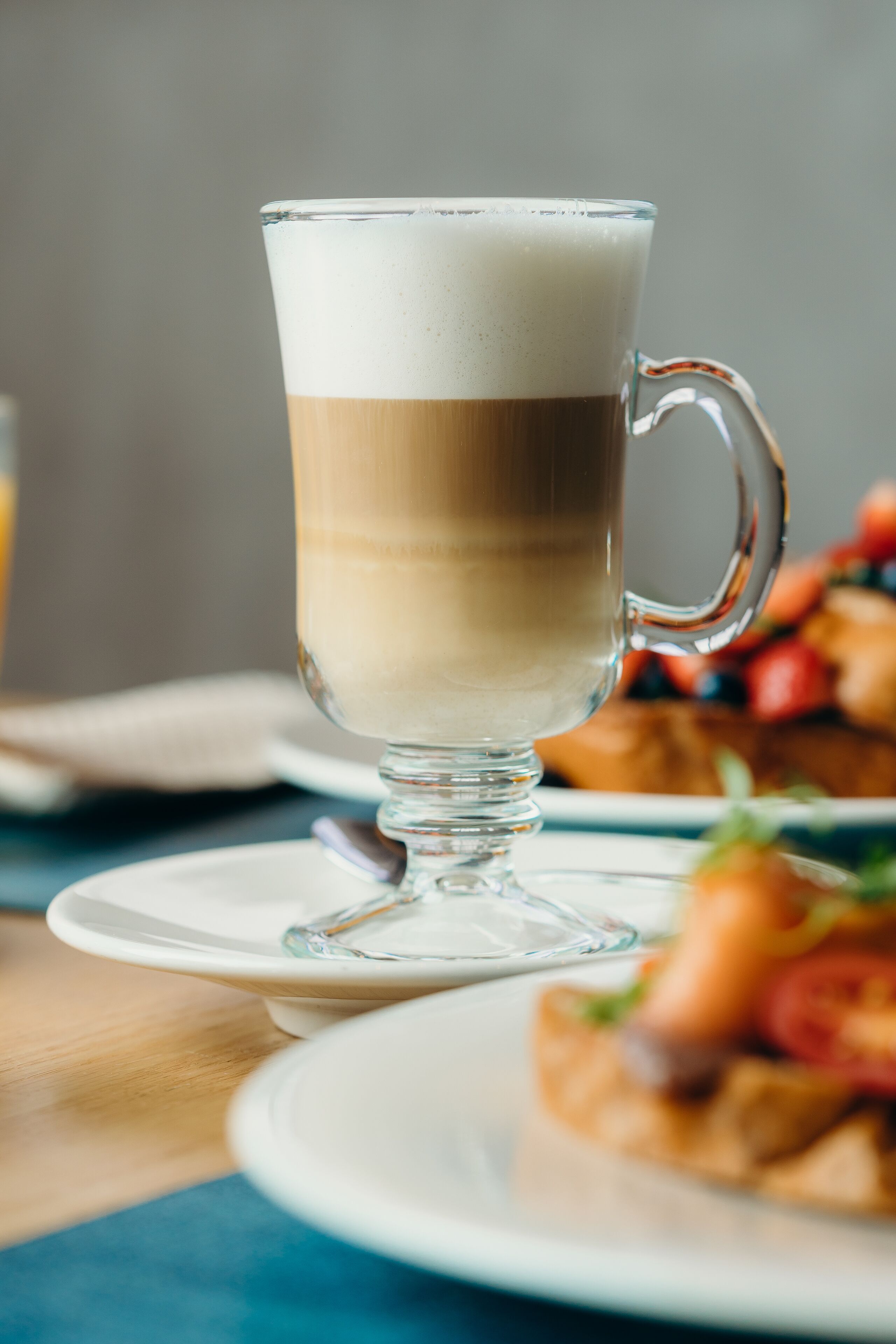 Un verre transparent contenant une boisson à plusieurs couches, une assiette avec de la nourriture et une serviette sur une table.
