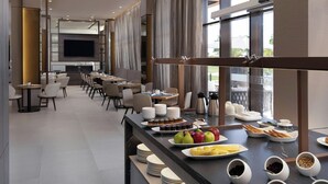 Un comedor moderno con una barra de buffet, que incluye frutas, pasteles y bebidas.
