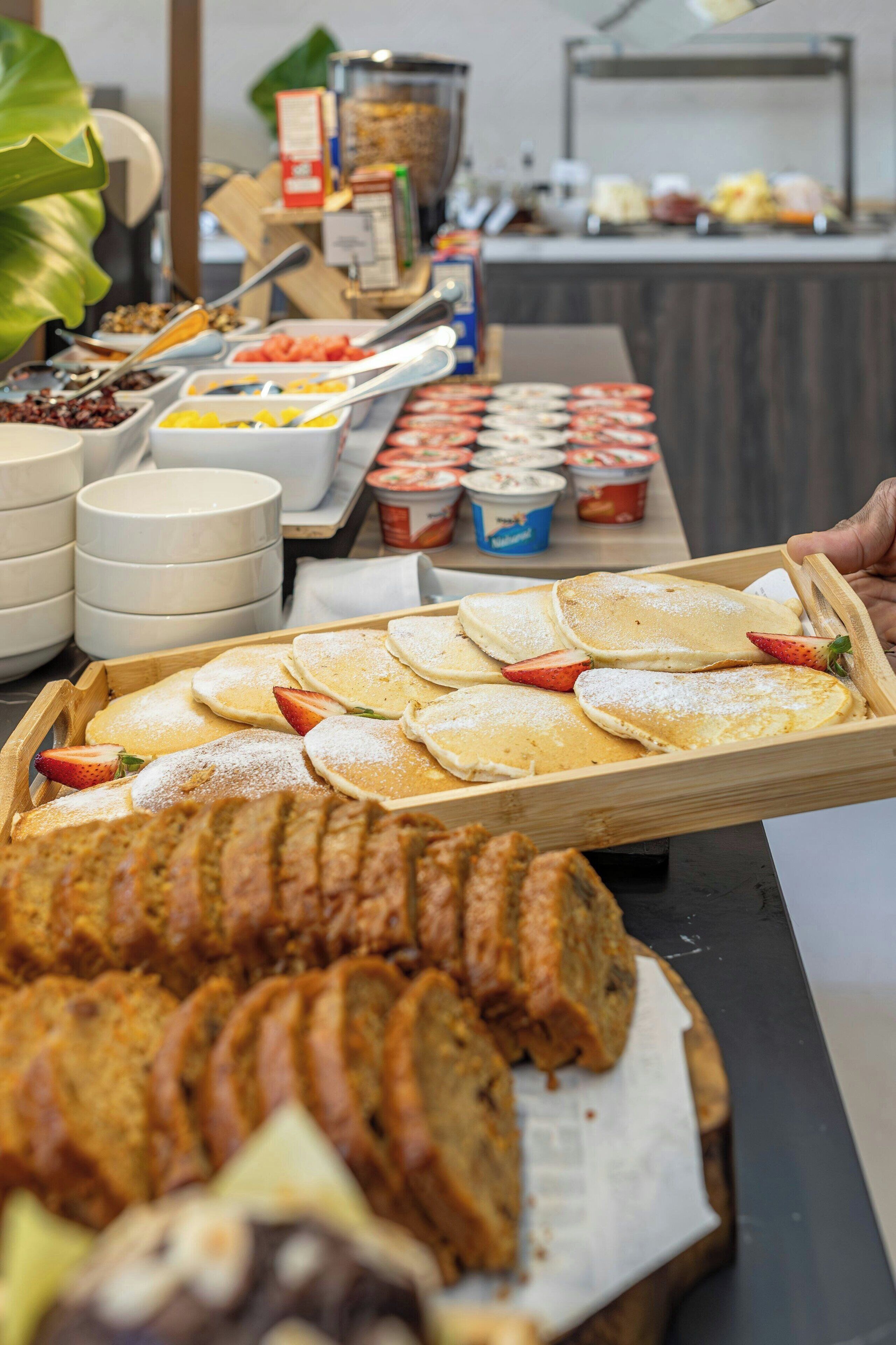 A buffet with various food items including pancakes, fruits, and desserts.