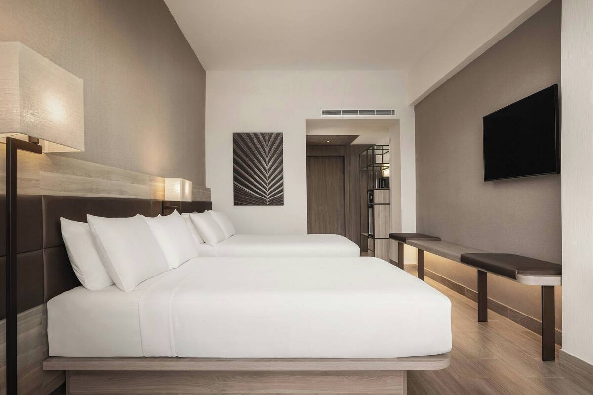 A modern hotel room with a large bed, bedside tables, a flat-screen TV, and a decorative wall piece.