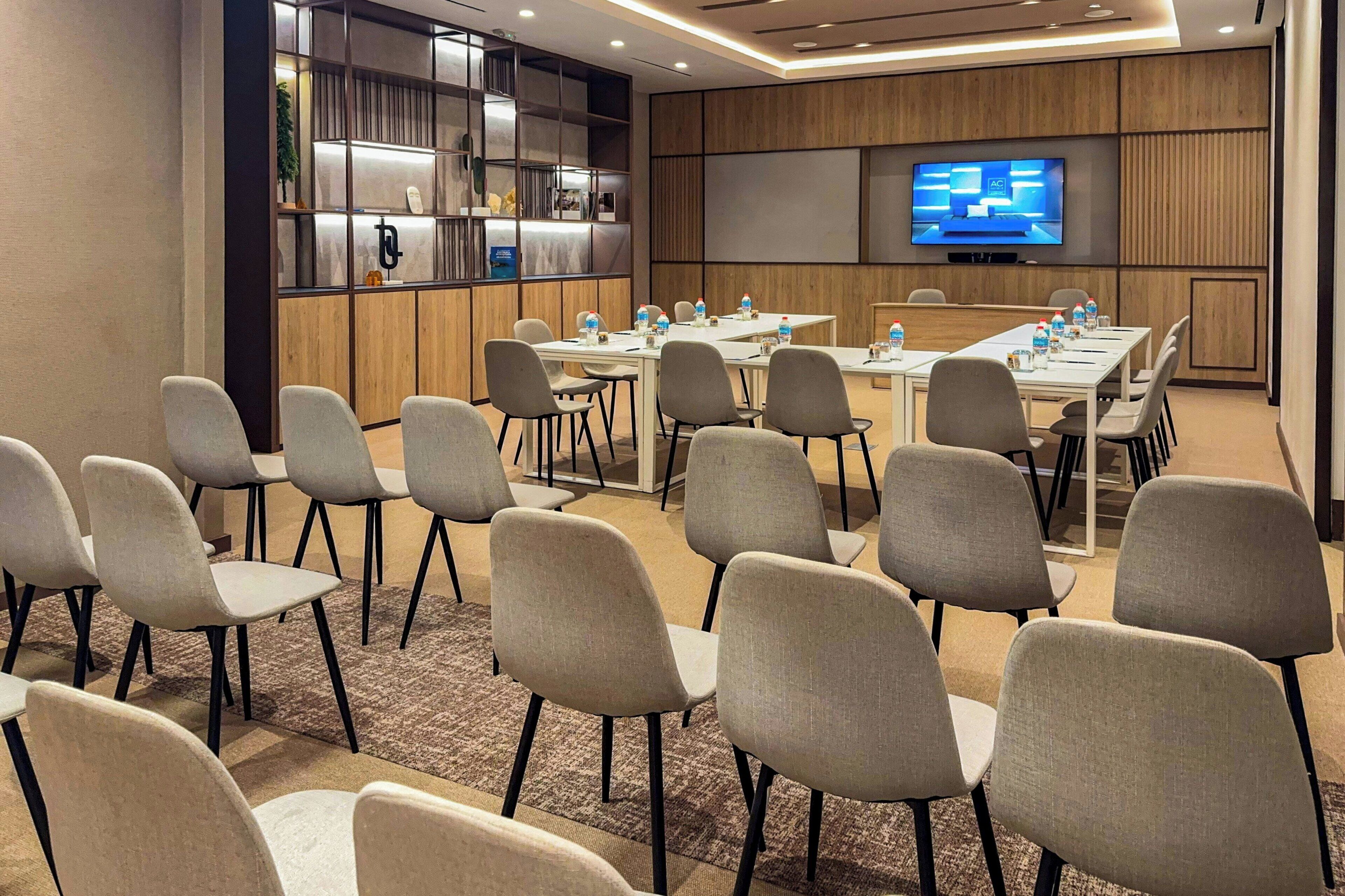 Un salón de conferencias con una mesa larga, sillas, un televisor y un armario con estantes.