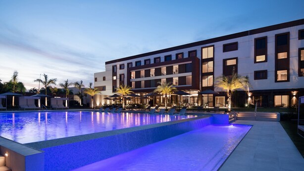 Un hotel moderno con piscina, zona de estar al aire libre y palmeras.