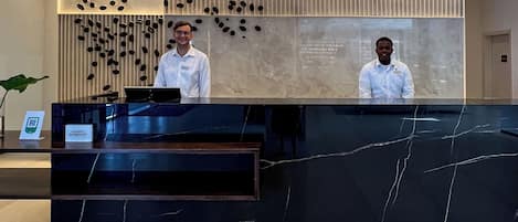 A reception desk with two staff members, a modern design with a marble top, and a vertical light strip above.