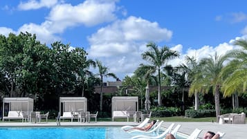 Una piscina con sillas de descanso y sombrillas, rodeada de palmeras y vegetación.