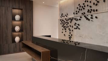 A modern reception area with a marble counter, wooden shelving with decorative vases, and a wall-mounted art piece with black oval shapes.