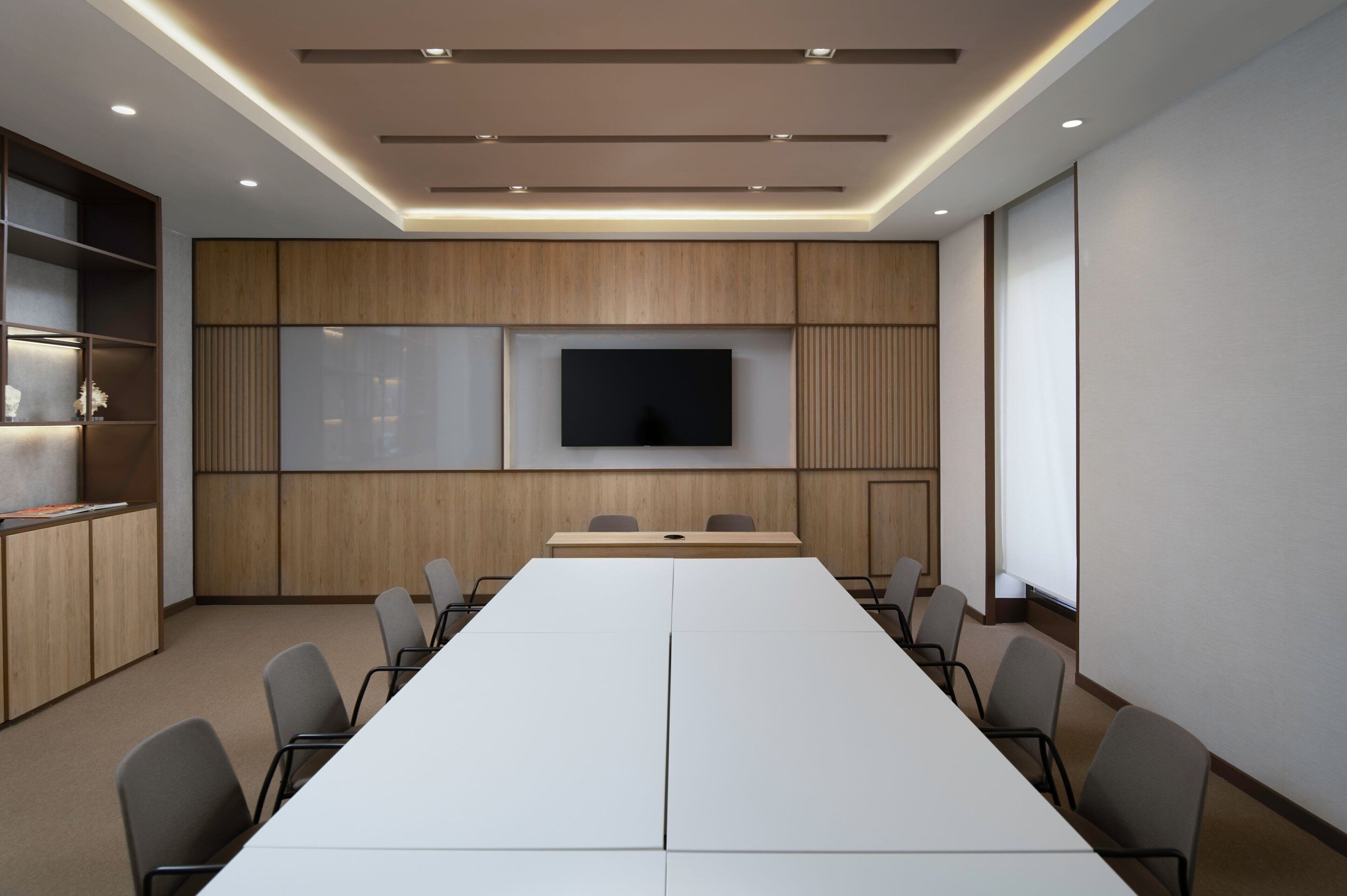 A conference room with a long table, chairs, a TV screen, and wooden paneling.