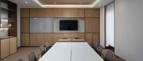A conference room with a long table, chairs, a TV screen, and wooden paneling.