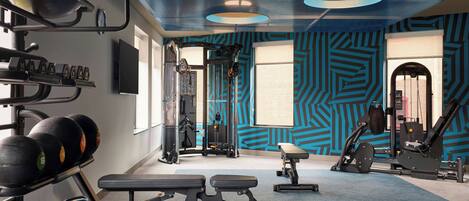 Un gimnasio con equipo de ejercicio, una banca y un pared con diseño.