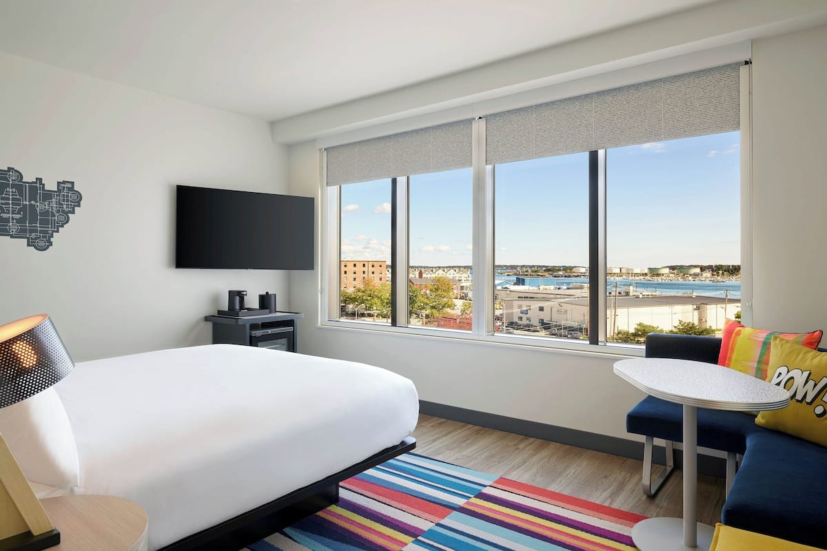 Ett hotellrum med en stor säng, ett litet bord, en soffa, en tv och ett fönster med utsikt över staden.