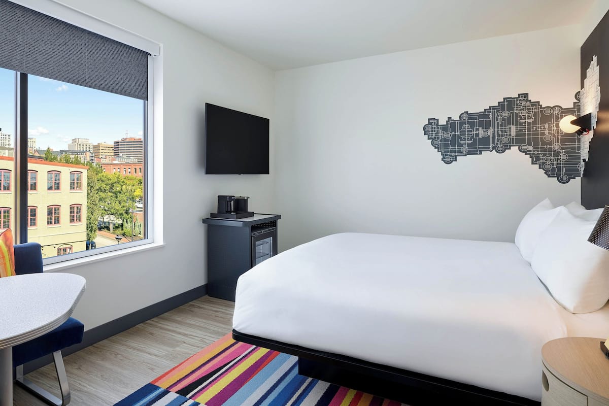 Ett hotellrum med ett stort fönster, en säng, ett skrivbord och en platt-TV.
