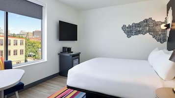 Une chambre d’hôtel dotée d’une grande fenêtre, d’un lit, d’un bureau et d’un téléviseur à écran plat.