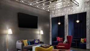 A modern living room with a grey sofa, a yellow armchair, and a red armchair. There are two floor lamps, a flat-screen TV, and patterned wallpaper. - Aloft by Marriott Portland Downtown Waterfront ME (Portland)