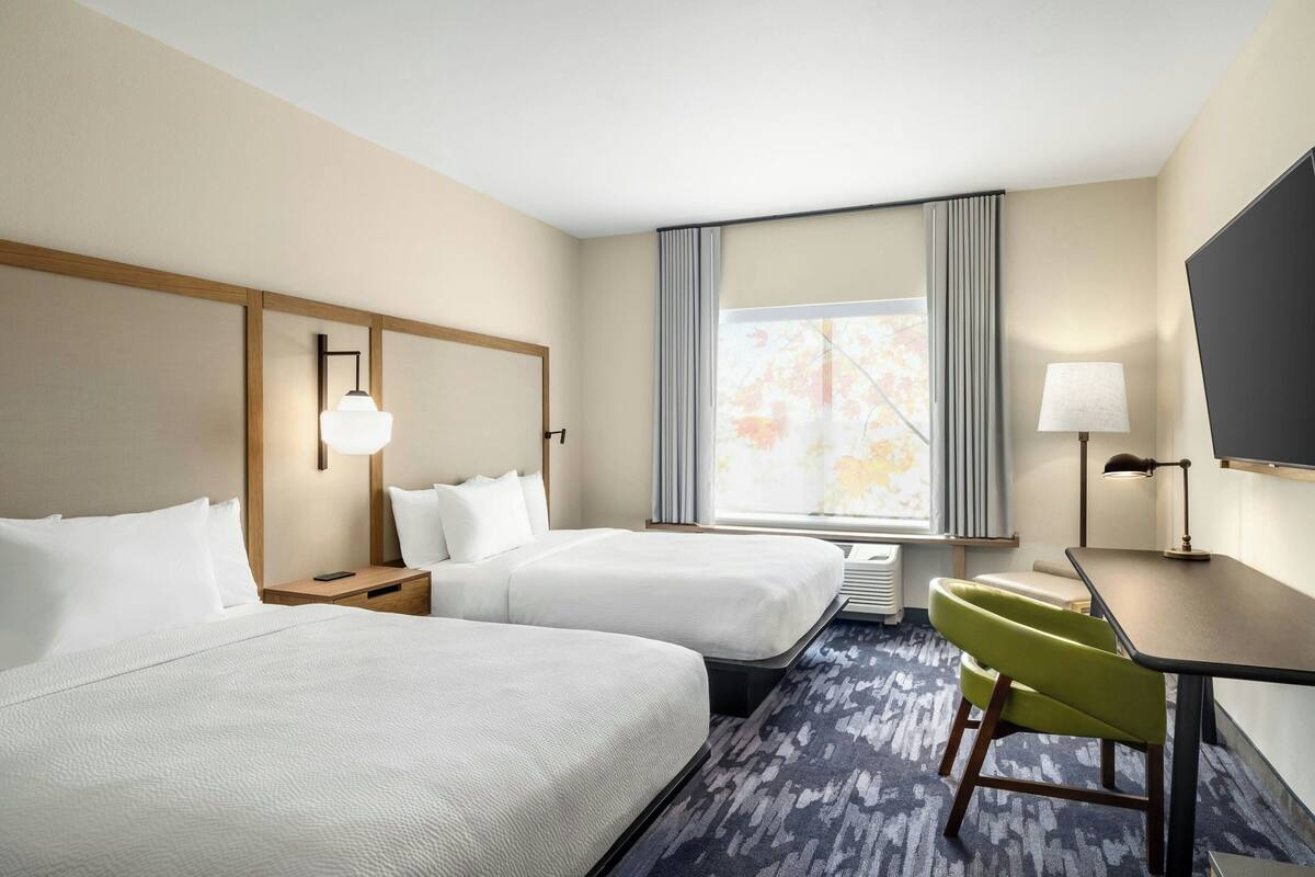 Une chambre d’hôtel avec deux lits, un bureau, une chaise, une télévision et une fenêtre avec des rideaux.