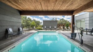 Une piscine dotée d’un plafond en bois, de chaises longues et offrant une vue sur des arbres et un bâtiment.
