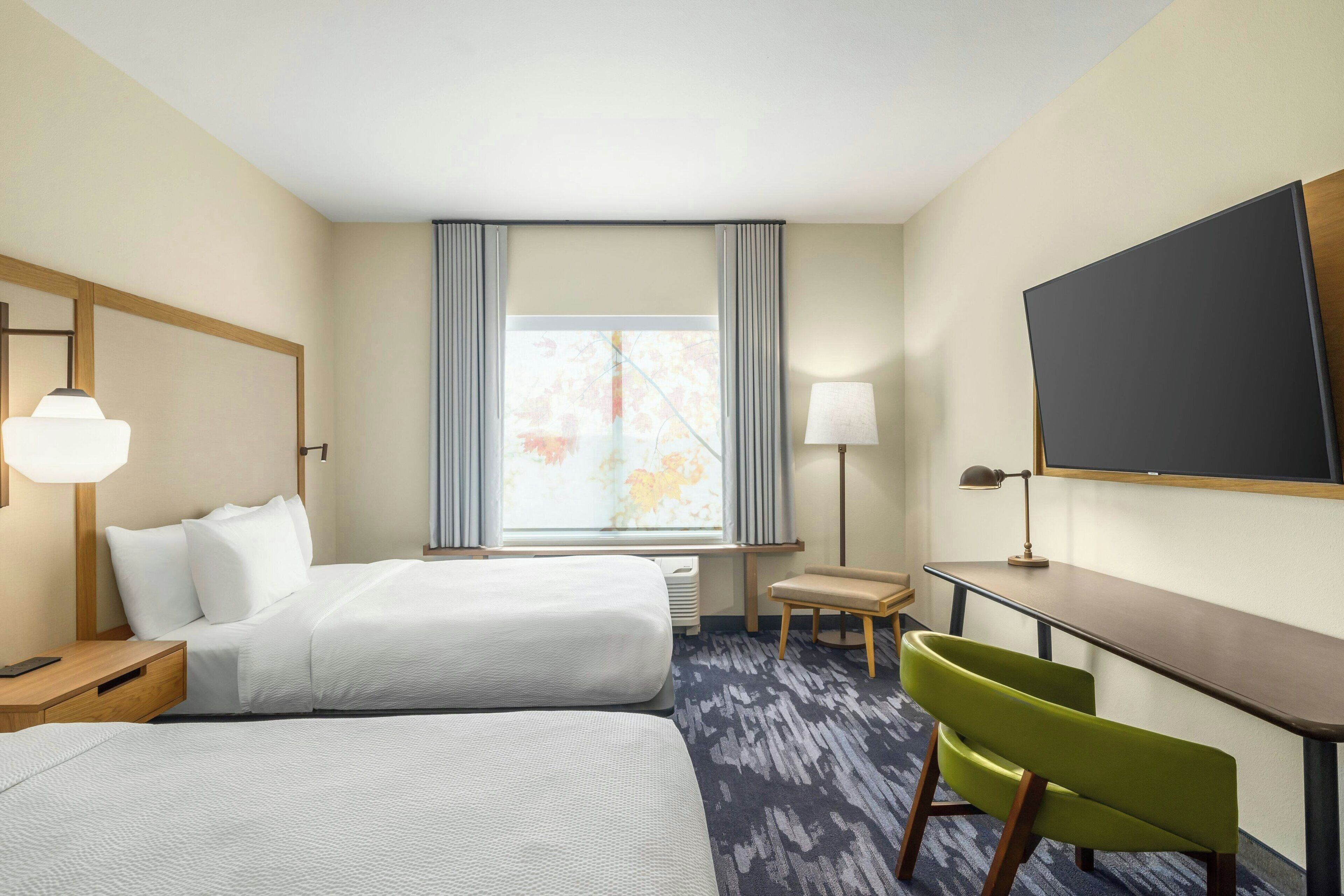 A hotel room with two beds, a desk, a chair, a TV, and a window with curtains.