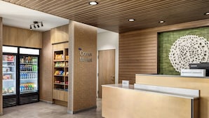Un espace d’accueil avec un comptoir de réception en bois, une enseigne indiquant « Corner Market » et un réfrigérateur rempli de boissons.