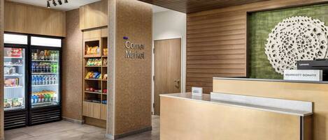 A reception area with a wooden reception desk, a 'Corner Market' sign, and a refrigerator stocked with beverages.